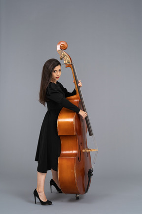 Side view of a serious young female musician in black dress playing her double-bass