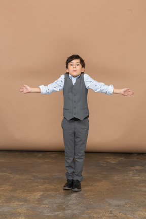 Vue de face d'un mignon garçon en costume debout avec les bras tendus