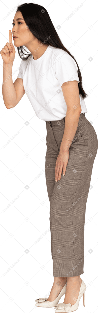 Vista di tre quarti di una giovane donna in calzoni e maglietta che mostra un gesto di silenzio