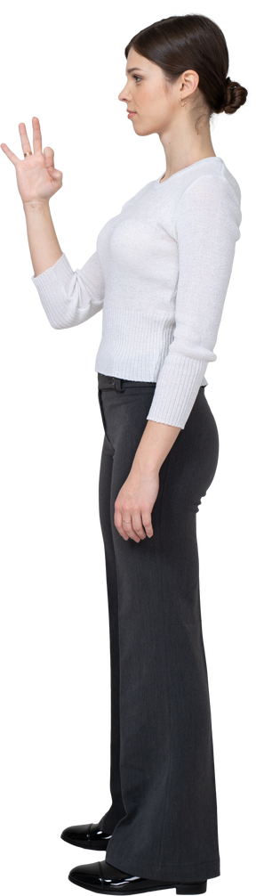 Side view of a young woman in office clothing showing ok sign