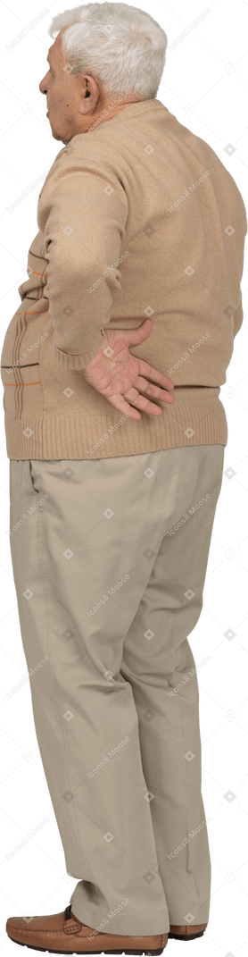 背中に手を置いて立っているカジュアルな服装の老人の側面図
