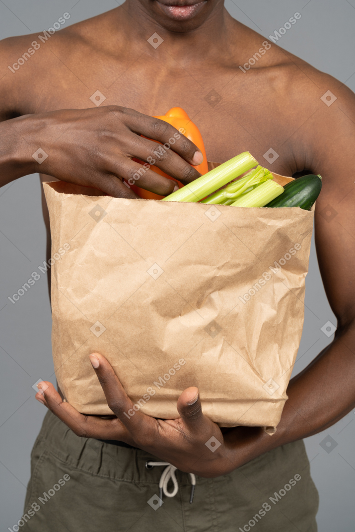 食料品の袋を保持している上半身裸の若い男