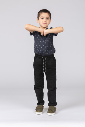 Front view of a cute boy posing with hands in front of chest and looking at camera