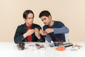 Dois jovens geeks sentado à mesa e consertando alguns detalhes