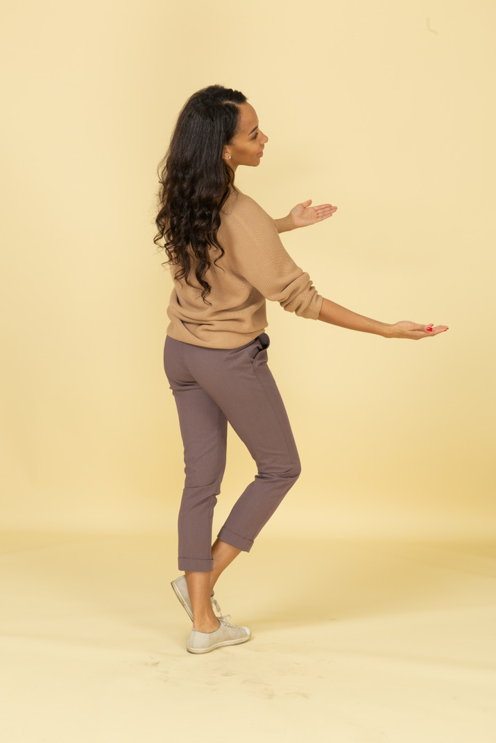 Three-quarter back view of a dark-skinned young female outstretching her hands