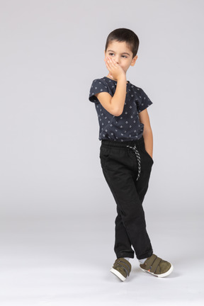 Вид спереди симпатичного мальчика в повседневной одежде, прикрывающего рот рукой