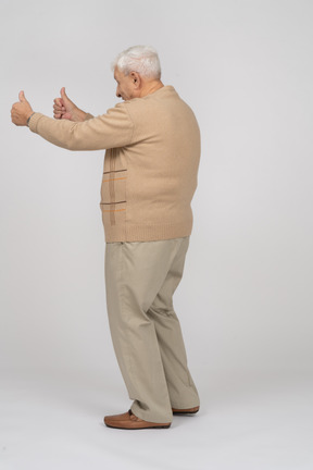 Vista lateral de un anciano feliz con ropa informal que muestra los pulgares hacia arriba