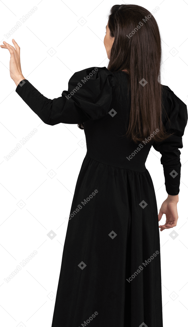 Rückansicht einer jungen dame in einem schwarzen kleid, die ihre hand hebt