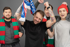 Close-up of four male football fans celebrating the victory & raising hands