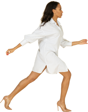 Vista lateral de uma jovem mulher de pele escura em um vestido branco dando um grande passo