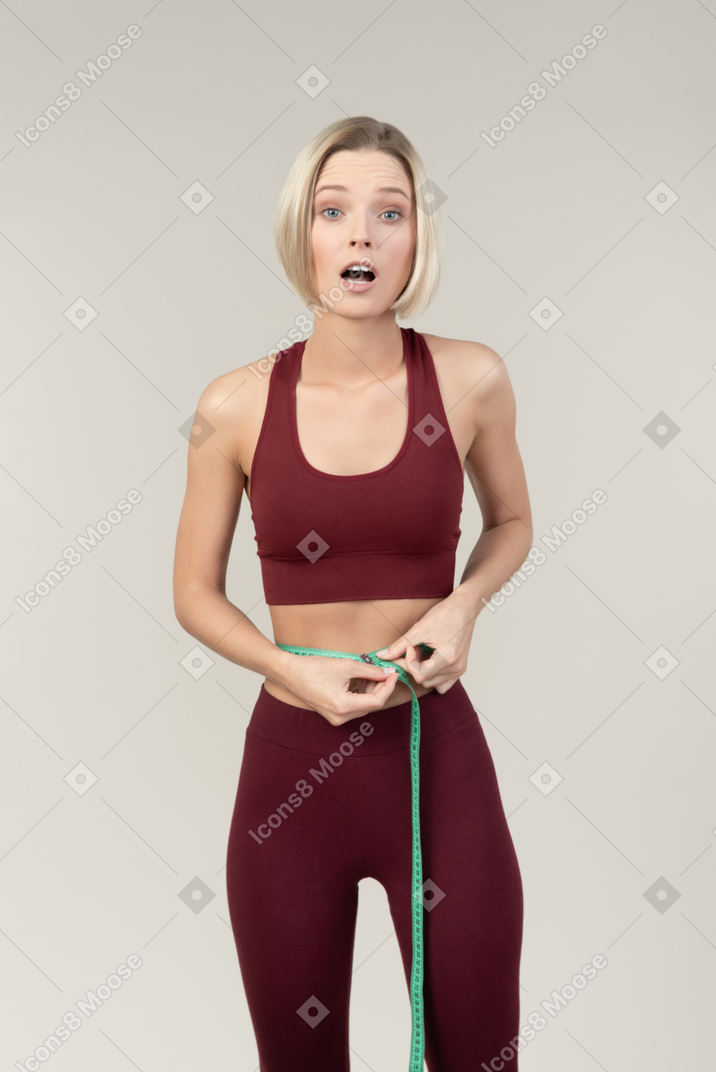 Amazed young woman in sportswear measuring waist