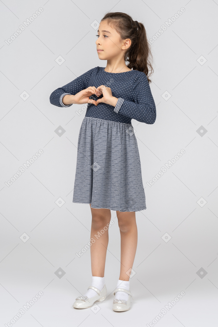 A little girl in a blue dress making a heart with hands