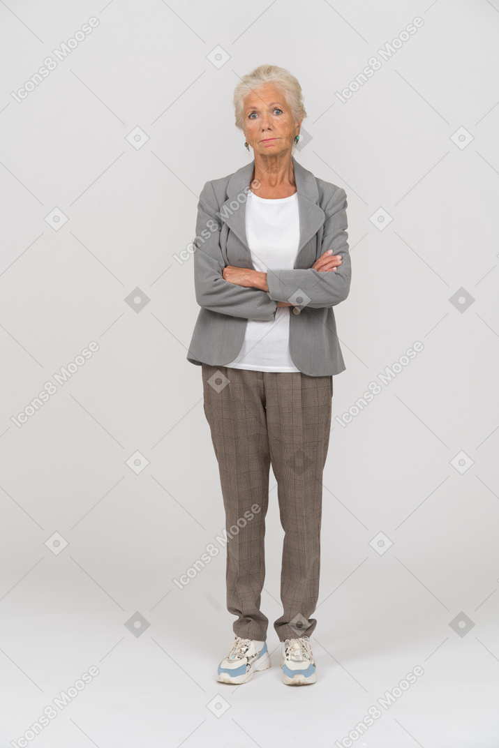 一个穿着西装的老妇人双臂交叉站立，看着相机的前视图