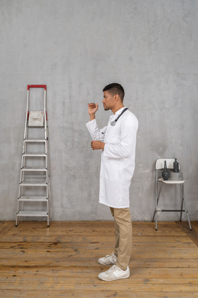 Side view of a young doctor standing in a room with ladder and chair showing a size of something