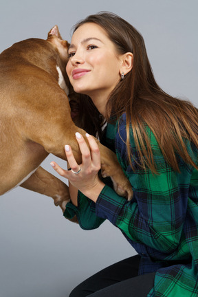 Vista laterale di una donna sorridente in camicia a quadri che abbraccia il suo bulldog