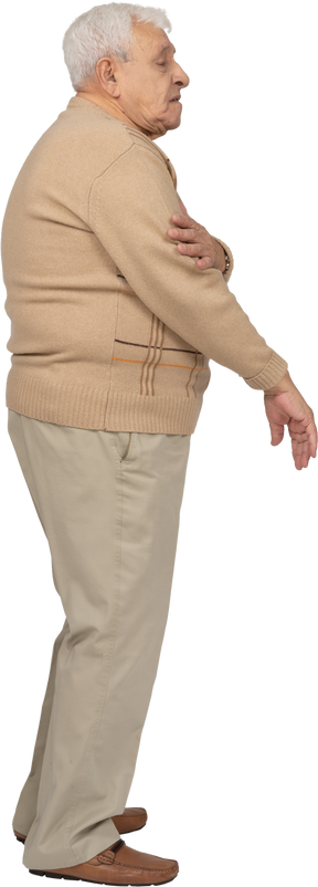 腕に手を置いて立っているカジュアルな服装の老人の側面図