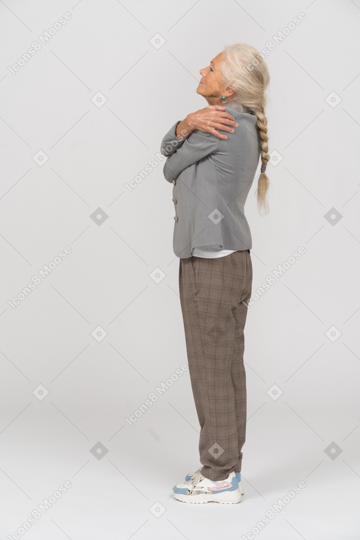 Side view of an old lady in suit hugging herself