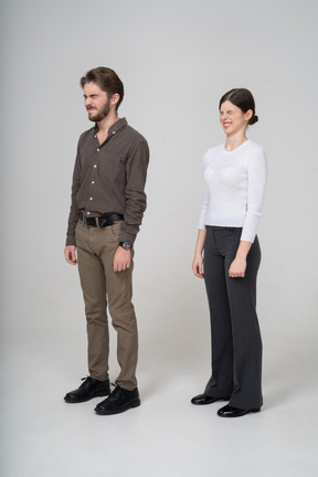 Vista de tres cuartos de una joven pareja disgustada haciendo muecas en ropa de oficina