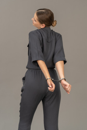 Трехчетвертный вид сзади страдающей молодой женщины в комбинезоне с наручниками