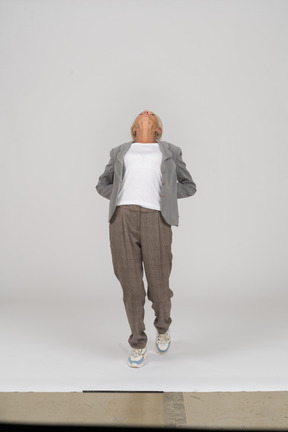 Vista frontal de una anciana en traje de pie con las manos detrás de la espalda y mirando hacia arriba