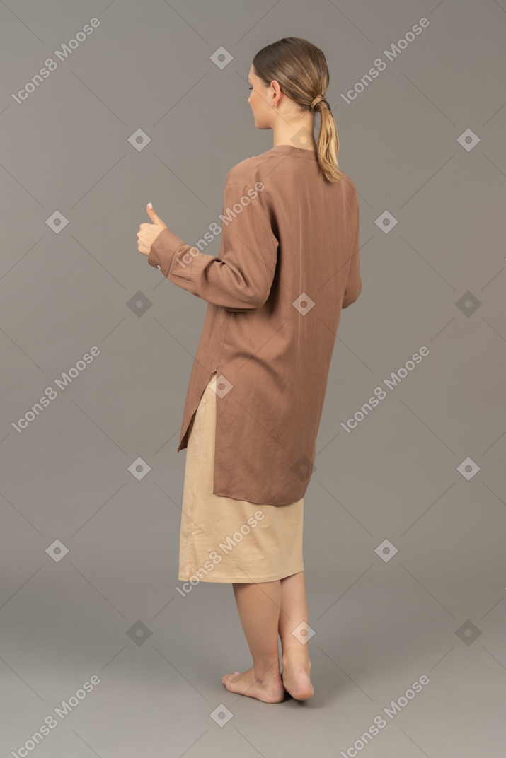 Vista de tres cuartos de una joven mujer descalza con los pulgares hacia arriba