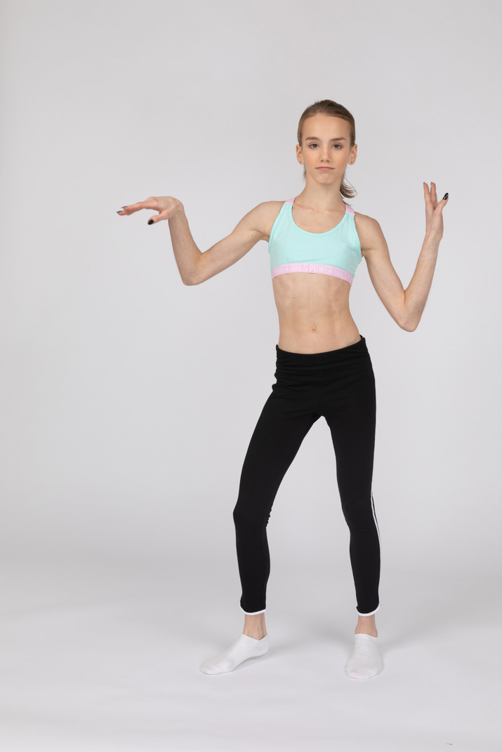 Front view of a teen girl in sportswear raising hands and dancing