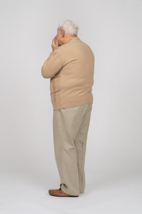 Vista lateral de un anciano con ropa informal cubriendo la boca con las manos