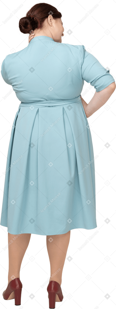 Rear view of a woman in blue dress posing with hand on hip