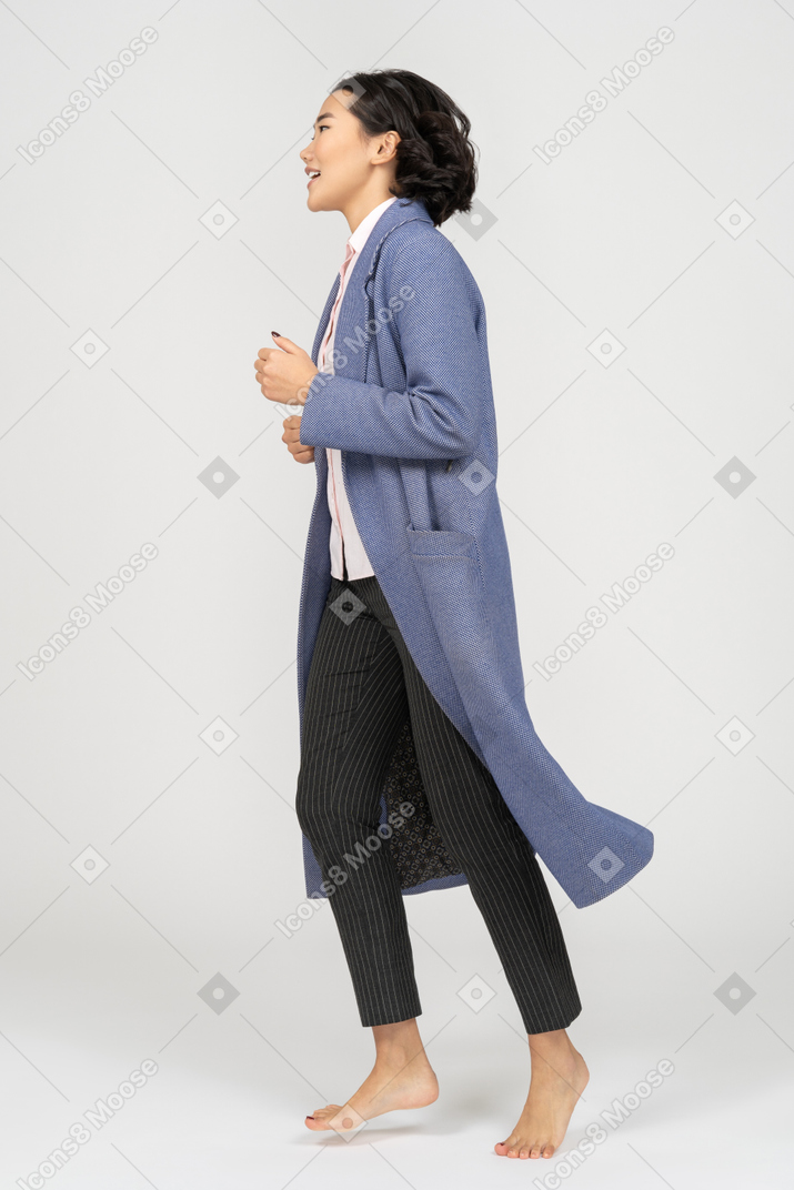 Вид сбоку улыбающейся женщины в пальто, бегущей