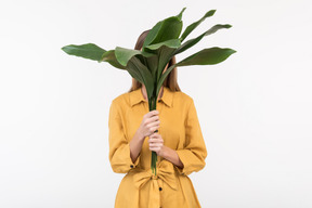 Young woman closing her face with big green leaves