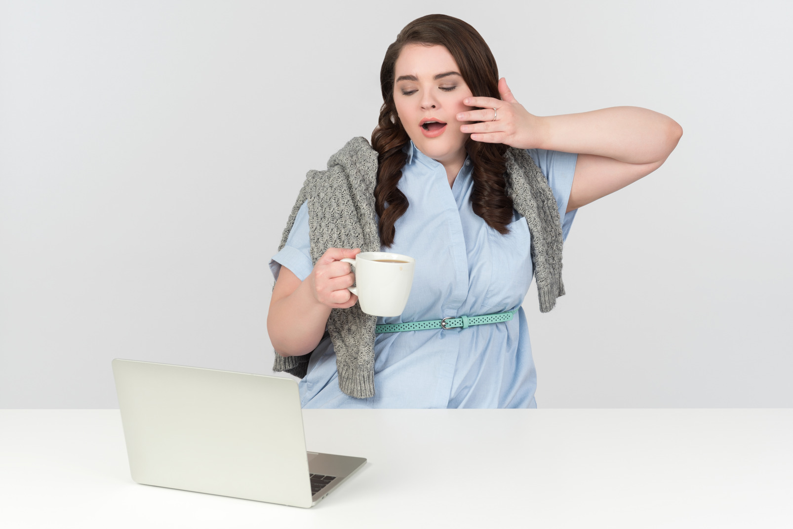 Young plus-size model yawning, drinking tea and looking at laptop