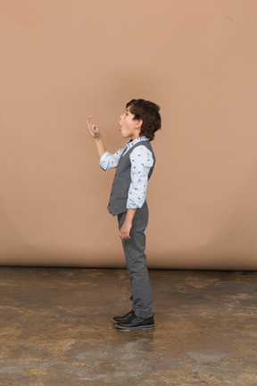 Vista lateral de un niño con traje gris que muestra el signo de ok