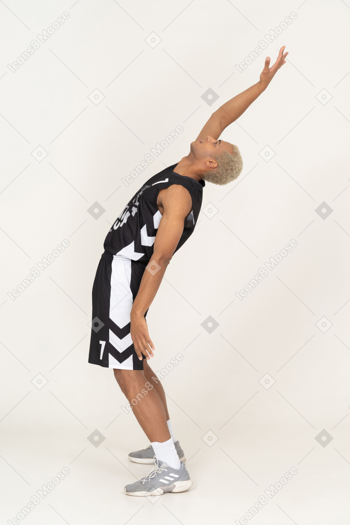 Вид сбоку молодого баскетболиста мужского пола, откидывающегося назад