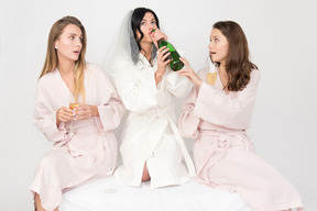 Brautjungfern, die versuchen, braut vom trinken der flasche champagners zu stoppen