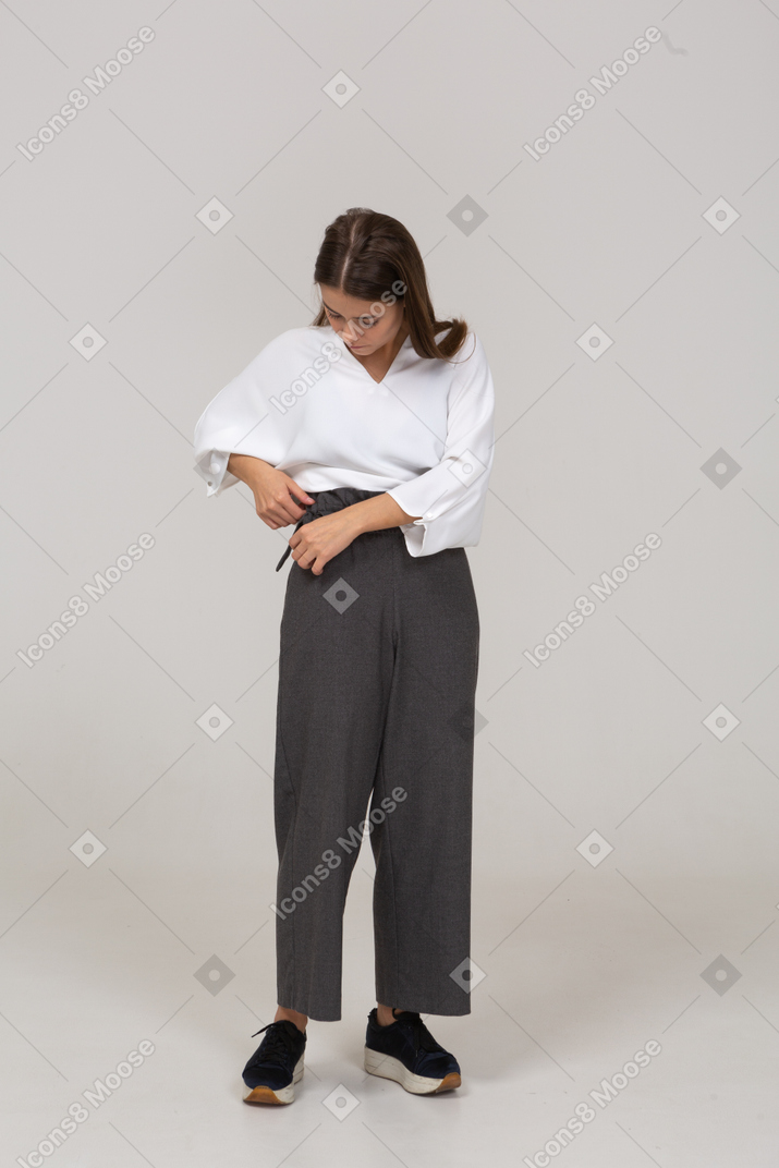 一位身着办公室服装的年轻女士调整裤子的前视图