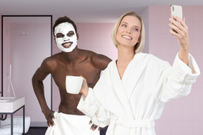 Girl making a selfie of her and her boyfriend with facial mask