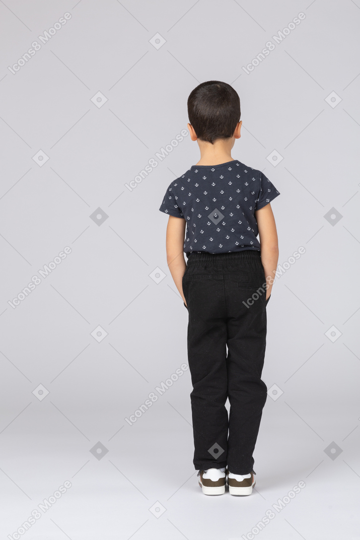 Вид сзади мальчика в повседневной одежде, стоящего с руками в карманах