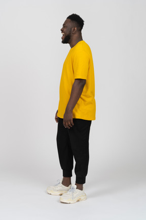 Vista laterale di un giovane uomo dalla pelle scura che ride in maglietta gialla