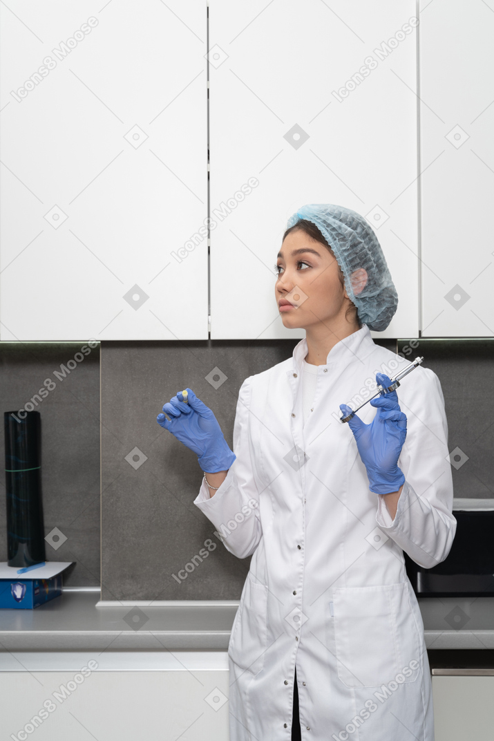 Three-quarter view of a nurse in her cabinet holding a syringe and looking aside