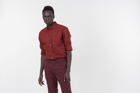 A young black man in a red shirt with rolled up sleeves and dark red pants standing alone on the white background