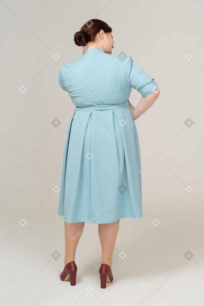Rear view of a woman in blue dress suffering from pain in neck