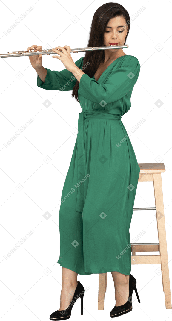 Comprimento total de uma jovem de vestido verde sentada em uma cadeira enquanto toca clarinete
