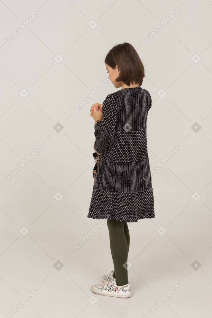 Vista posteriore di tre quarti di una bambina triste in abito che si tiene per mano insieme