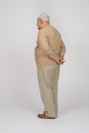 Seitenansicht eines alten mannes in freizeitkleidung, der mit den händen hinter dem rücken posiert