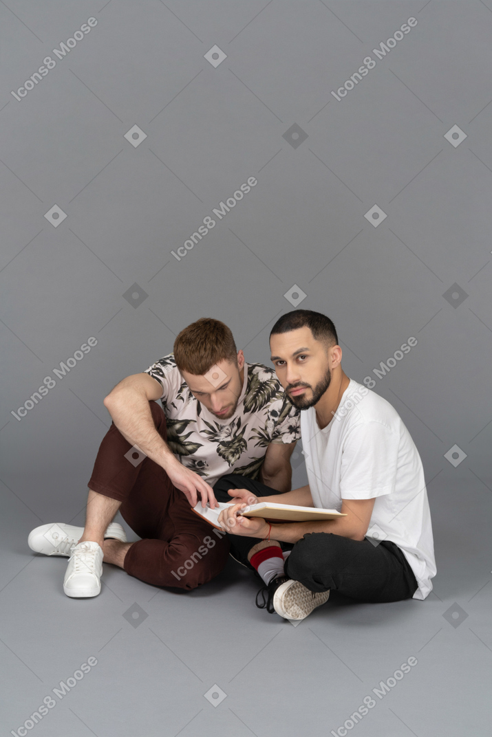 Vista di tre quarti di due giovani uomini seduti per terra a leggere