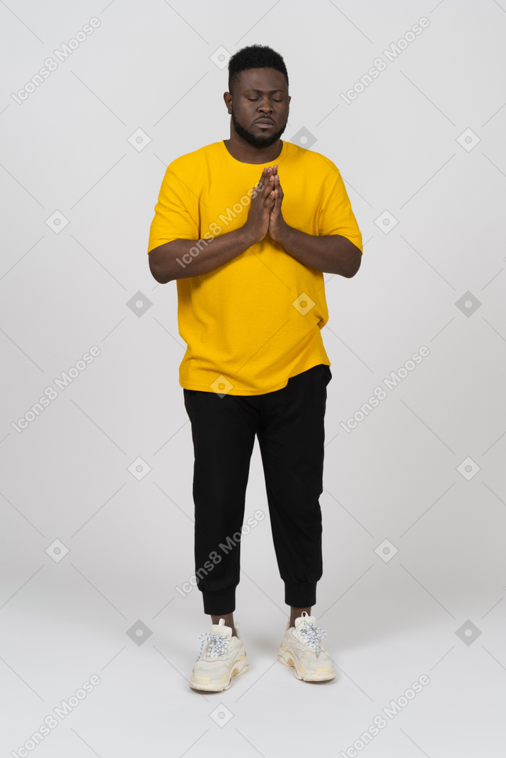 Vorderansicht eines betenden jungen dunkelhäutigen mannes in gelbem t-shirt, das händchen hält