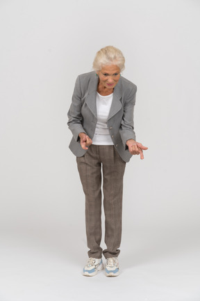 Vista frontal de uma senhora idosa de terno se abaixando e explicando algo