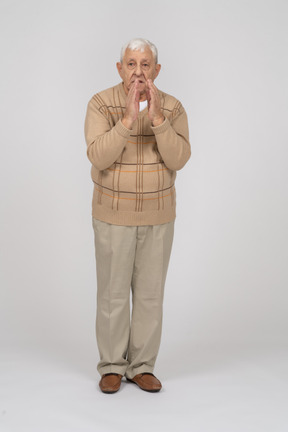 Front view of an old man in casual clothes holds hands in praying gesture