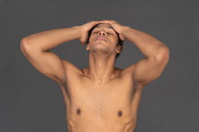 Vista frontal de um homem afro sem camisa tocando sua cabeça