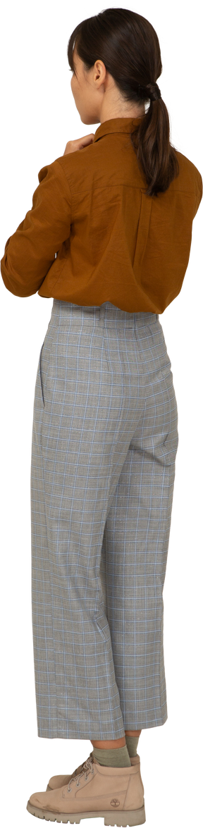 Vista posteriore di tre quarti di una giovane donna asiatica in calzoni e camicetta che si tiene per mano insieme